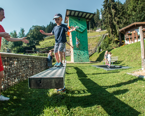 Kinder spielen gemeinsam auf einer Wiese im Außenbereich einer Ferienanlage.