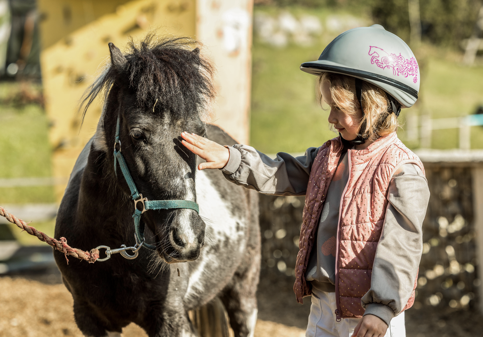 Kind führt ein Pony auf einem Bauernhofgelände.