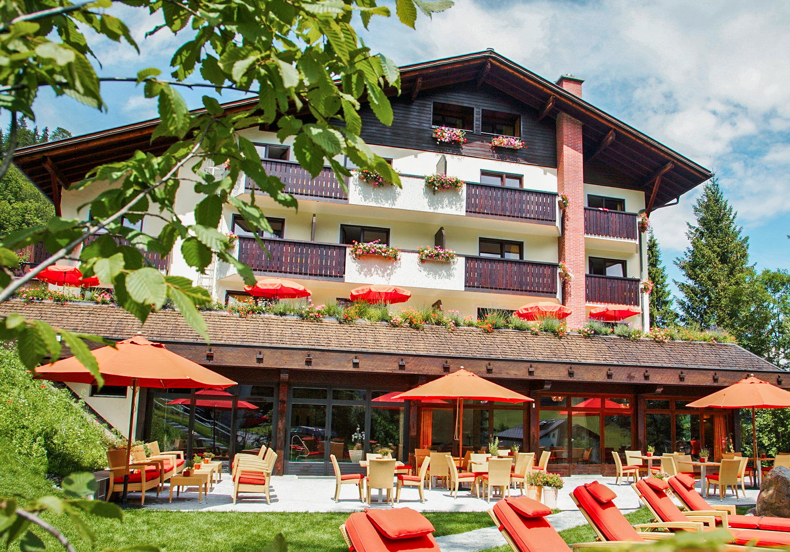 Hotelgebäude mit Balkonen und Sonnenterrasse in alpiner Umgebung.