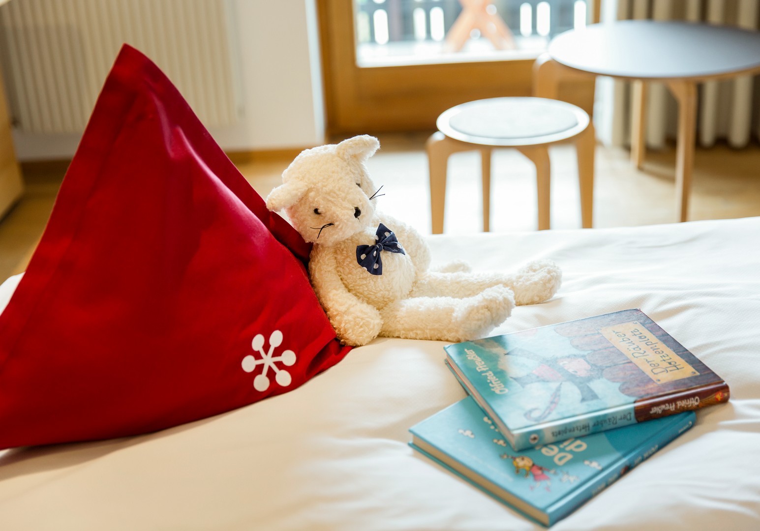 Kuscheltier lehnt an einem roten Kissen auf einem Bett.