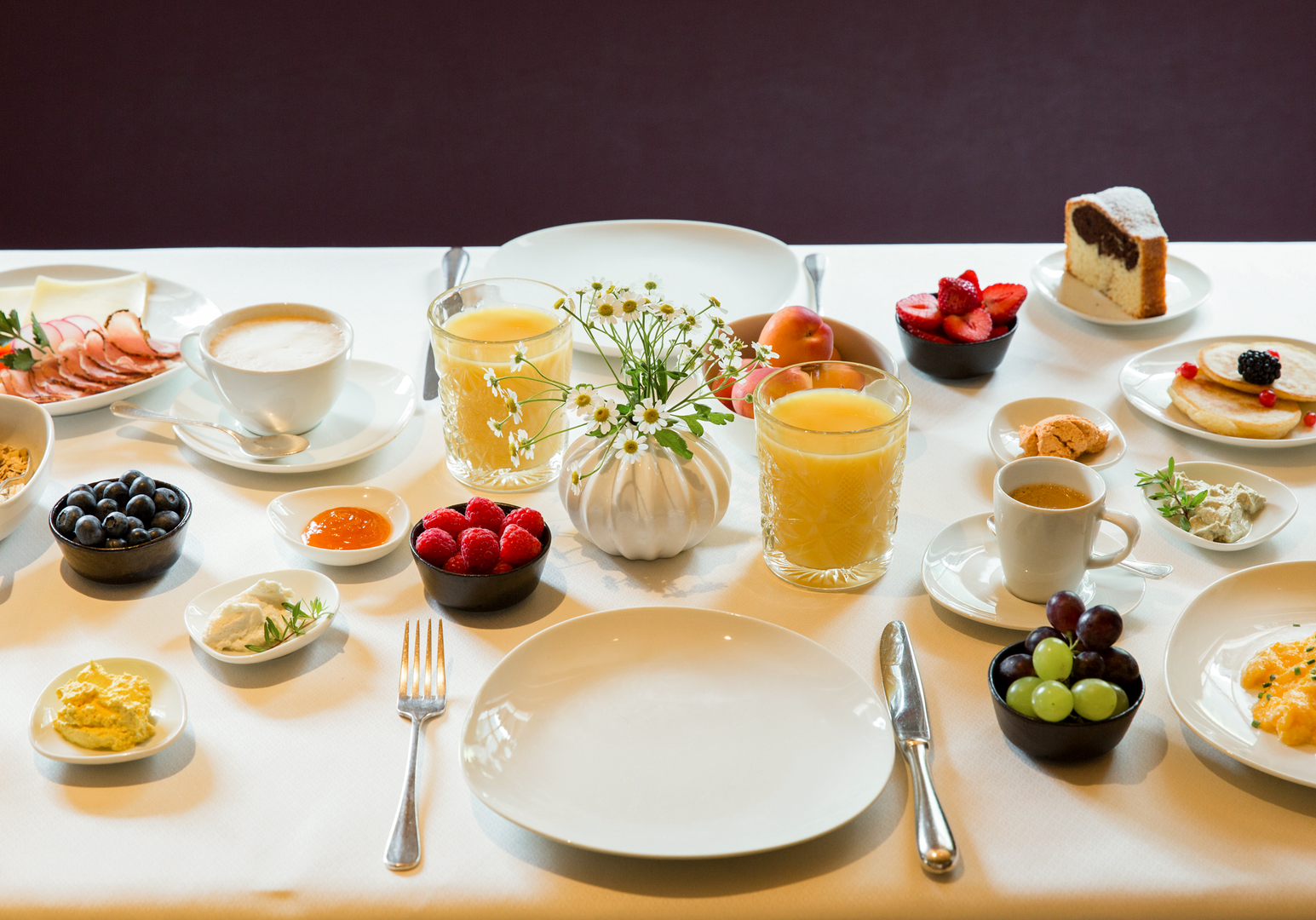 Frühstückstisch mit verschiedenen Speisen, Obst und Getränken.
