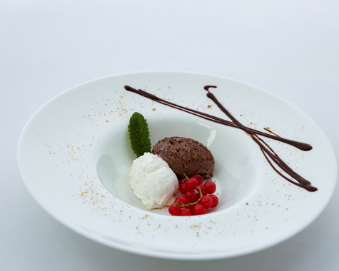 Schokoladendessert mit roten Beeren auf weißem Teller, daneben dekorative Schokoladenstäbchen.