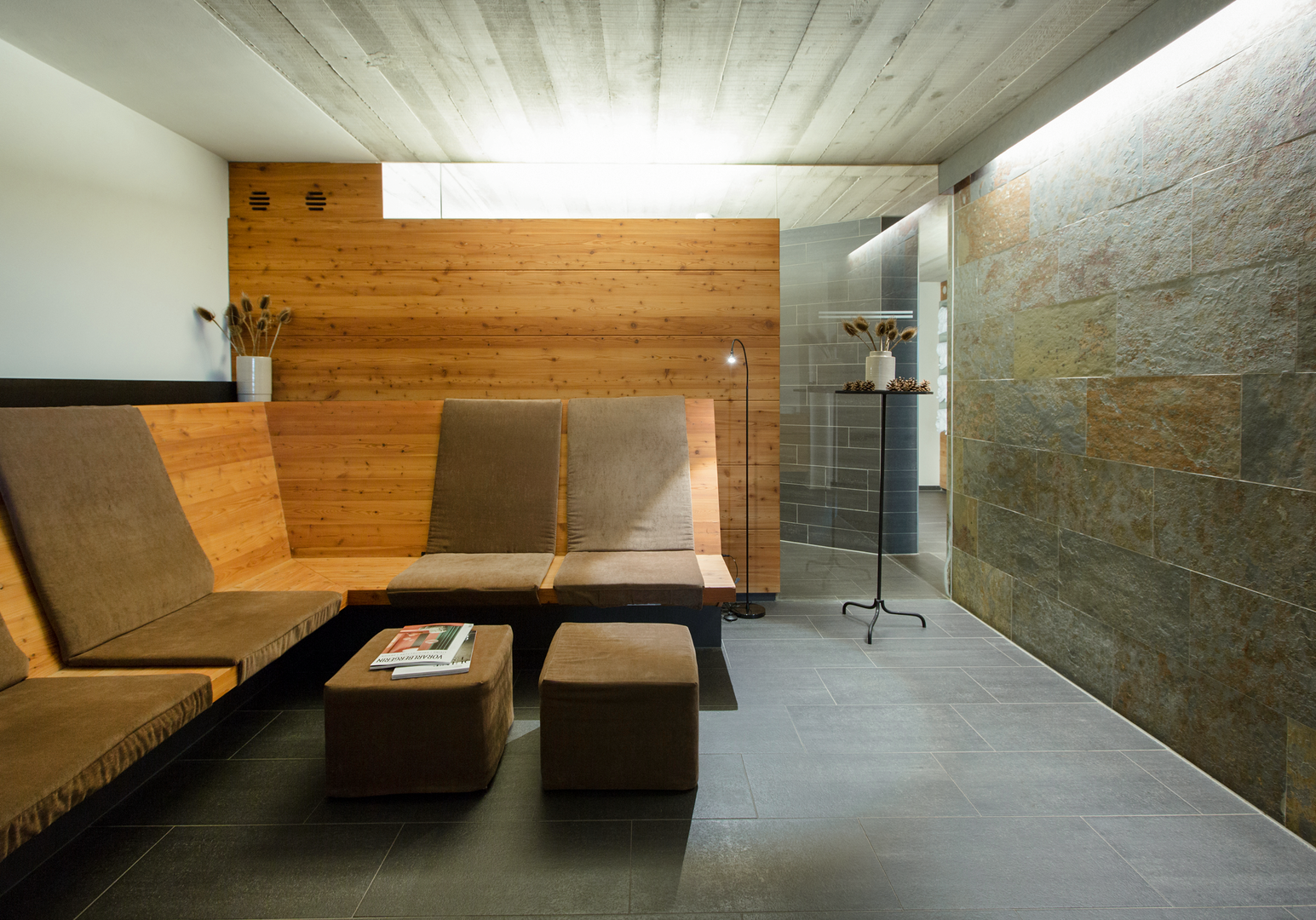 Ruheraum im Wellnessbereich mit Liegen, Holzverkleidung und Blick auf die Sauna.