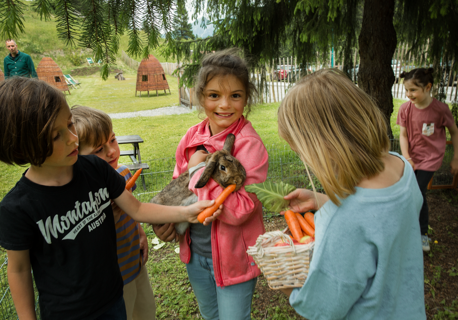 Kind hat ein Kaninchen auf dem Arm und andere Kinder füttern es mit Karotten. 