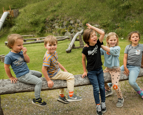 Kinder sitzen lachen auf einem Holzbalken. 