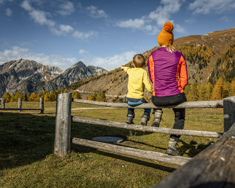 Erwachsener und Kind sitzen auf einem Holzzaun und genießen den Blick auf die Berge.
