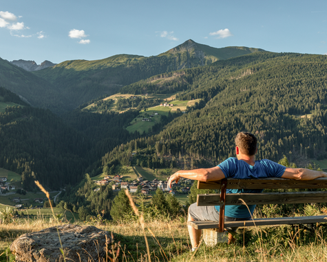 Person genießt die Aussicht auf die Alpen von einer Holzbank. 