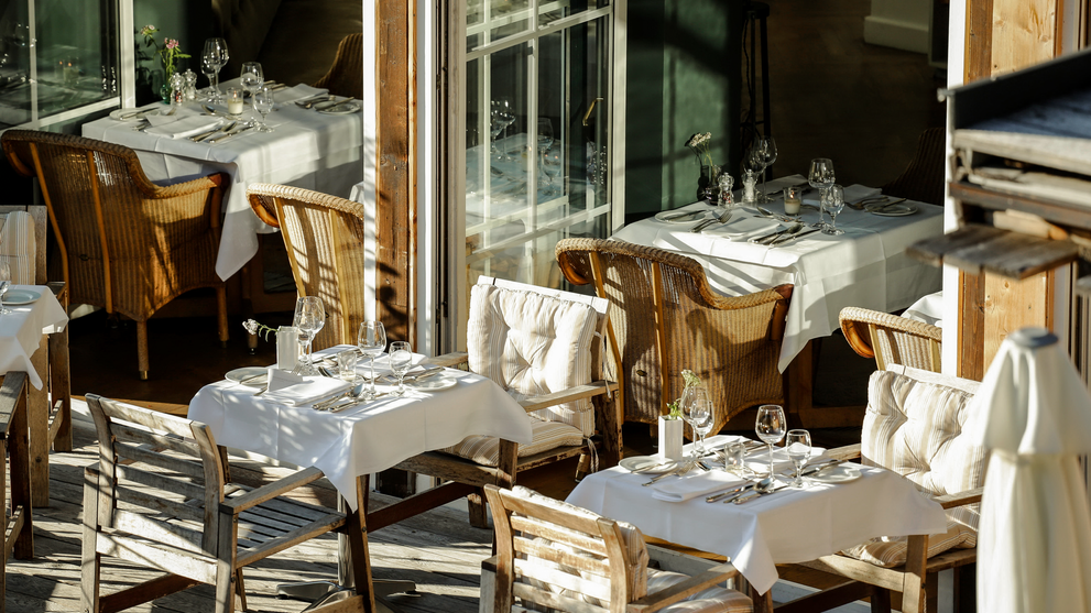 Gedeckte Tische auf einer sonnigen Restaurantterrasse mit Blick ins Grüne.