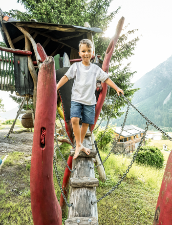 Kind erkundet einen naturnahen Spielbereich mit Kletter- und Balancierelementen.