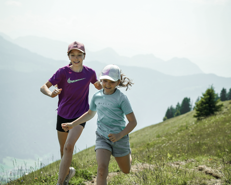 Erwachsener und Kind wandern gemeinsam über eine Bergwiese.