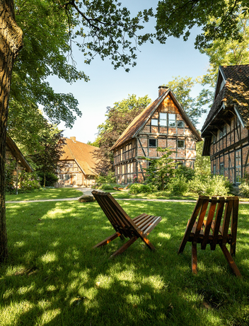 Garten mit Liegestühlen unter Bäumen vor Fachwerkgebäuden