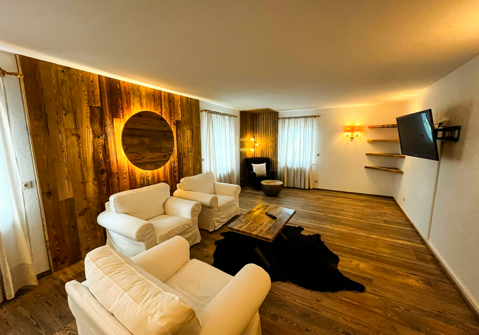 Wohnbereich mit weißen Sofas, rundem Spiegel und Holzwand