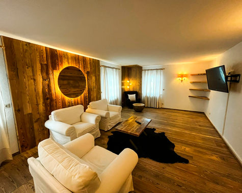 Wohnbereich mit weißen Sofas, rundem Spiegel und Holzwand