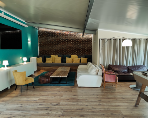Lounge mit verschiedenen Sitzmöbeln, TV und langen Vorhängen