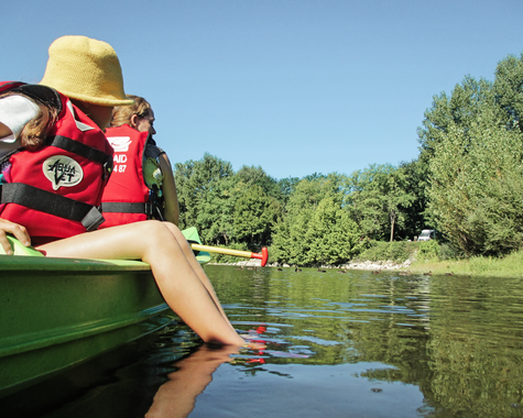 Person sitzt in einem Kajak und streckt die Füße ins Wasser auf einem ruhigen Fluss