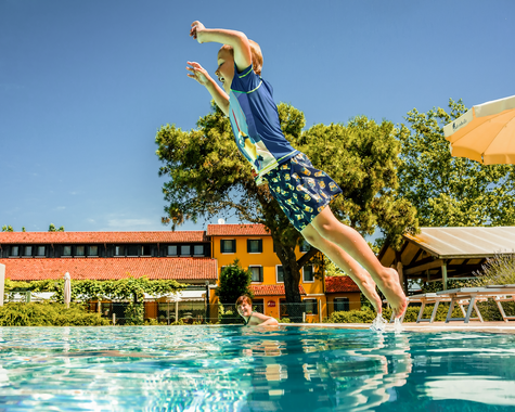 Kind springt in den Swimmingpool der Ferienanlage.