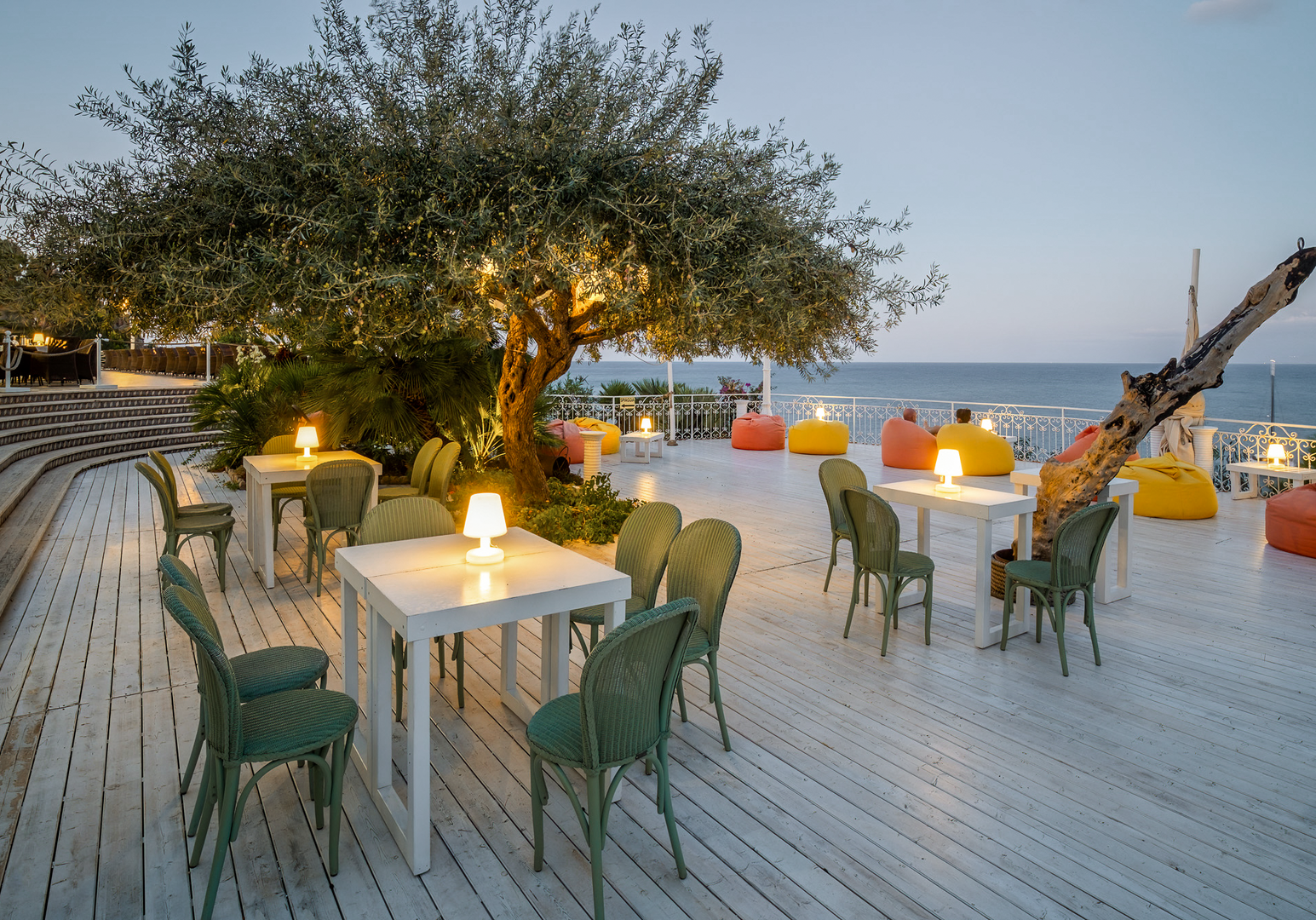 Gedeckte Tische auf einer Terrasse direkt am Meer in stimmungsvoller Abendatmosphäre.