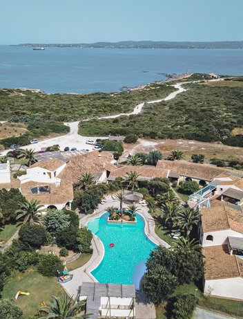 Blick über eine Ferienanlage mit Pool und Meer am Horizont 