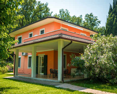 Freistehendes Ferienhaus mit überdachter Terrasse, umgeben von Bäumen und mediterraner Vegetation.