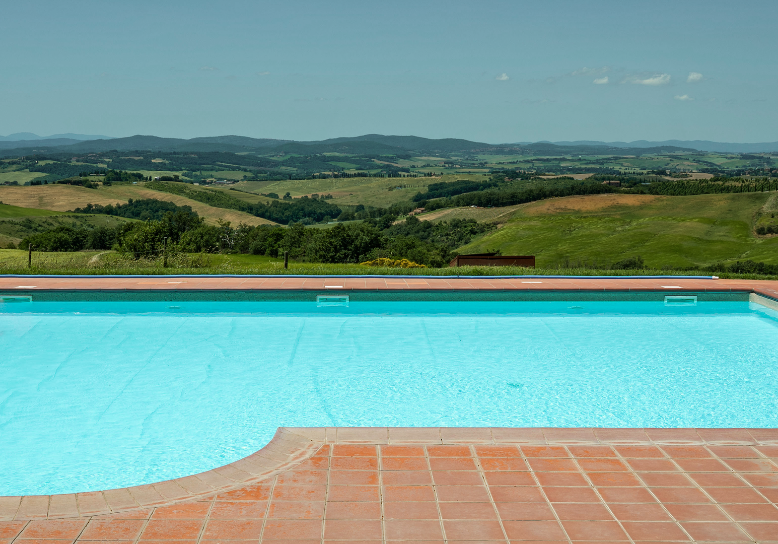 Sonnenterrasse am Pool mit freiem Blick über Felder und sanfte Hügel.
