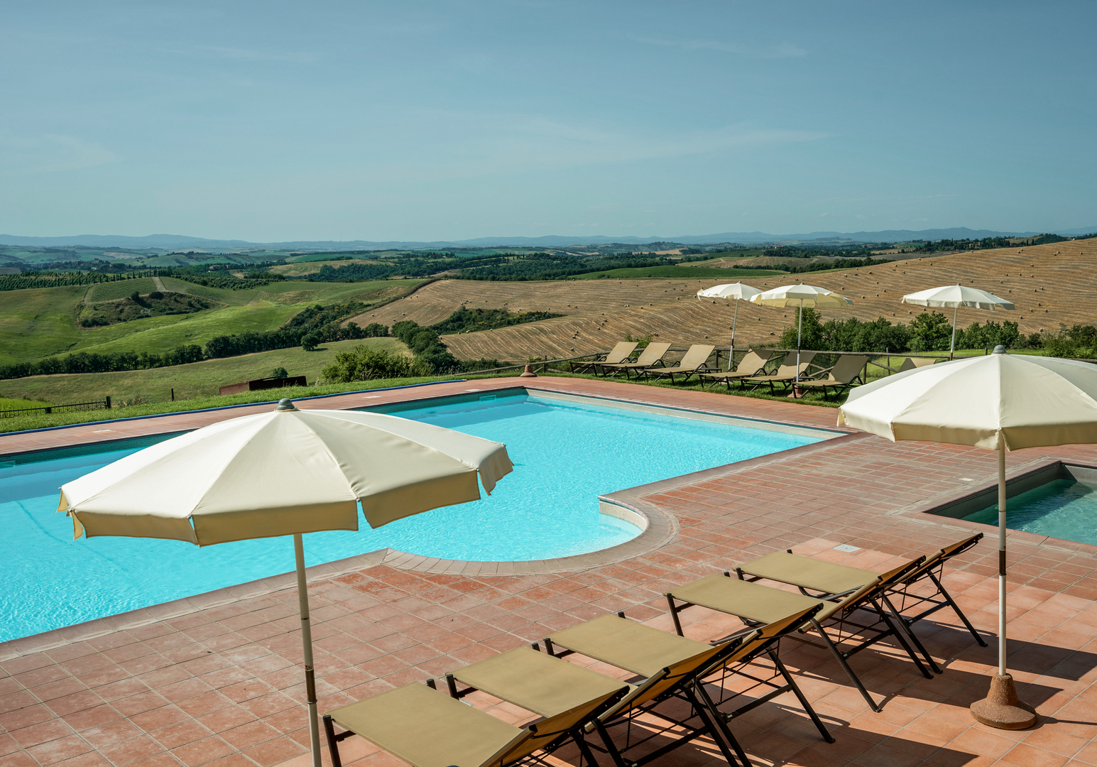 Infinity-Pool mit Sonnenschirmen und Liegen vor einer weiten Hügellandschaft.
