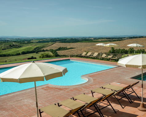 Infinity-Pool mit Sonnenschirmen und Liegen vor einer weiten Hügellandschaft.