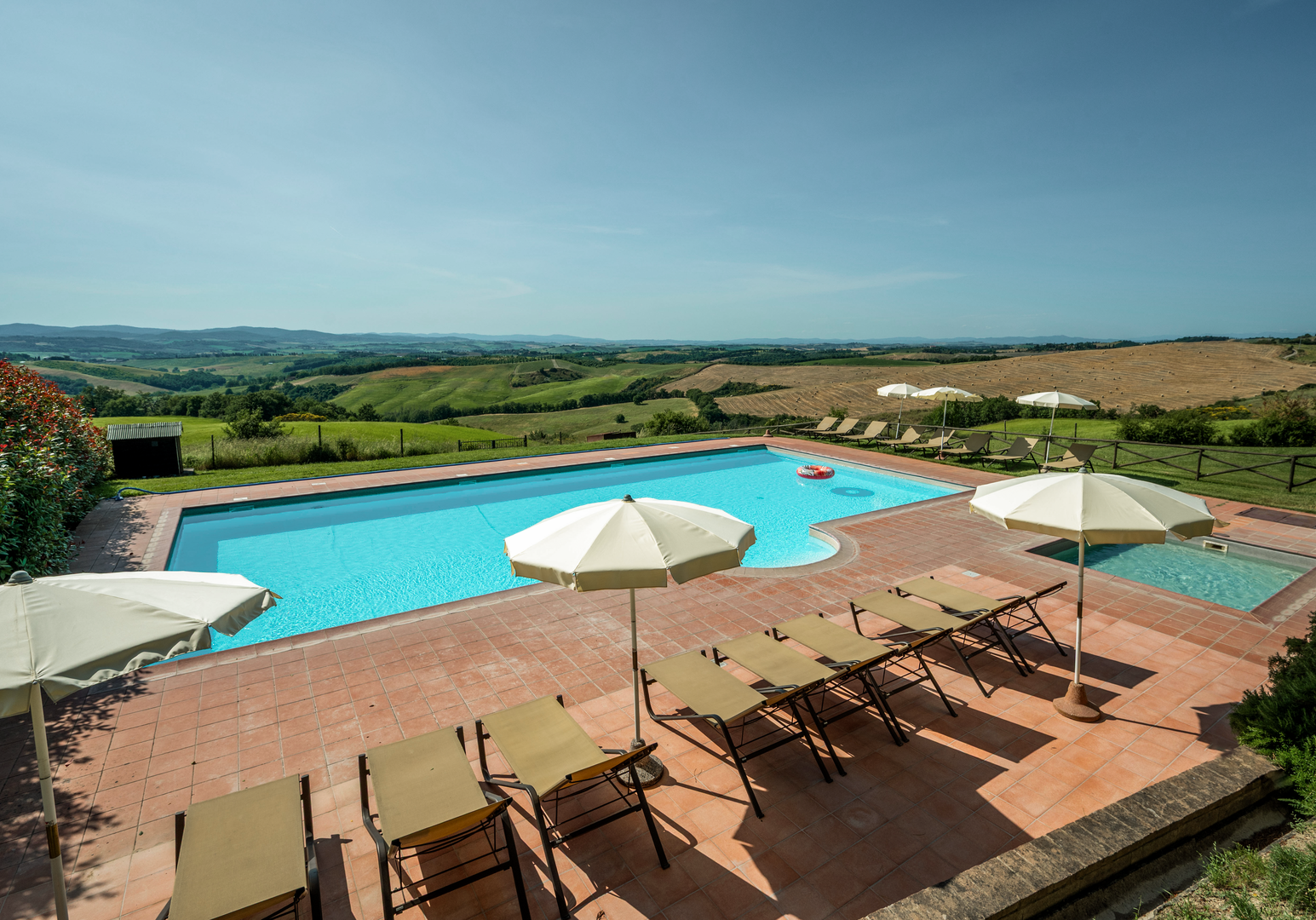Sonnenterrasse mit Pool, Liegen und freiem Blick über Felder und sanfte Hügel.