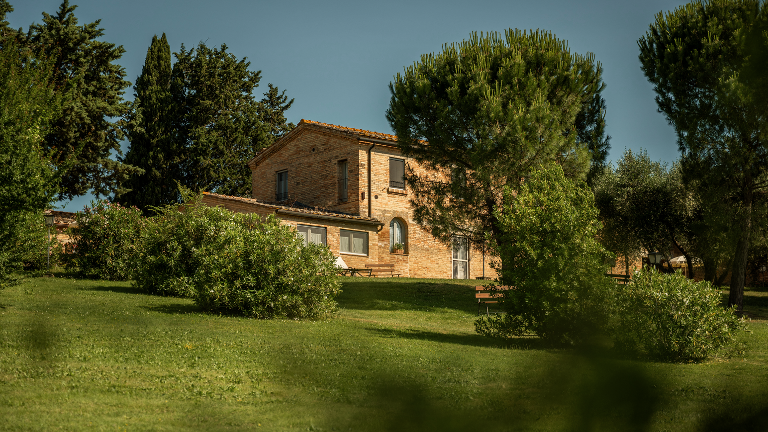 Landhaus umgeben von gepflegten Rasenflächen, Bäumen und mediterranen Pflanzen.