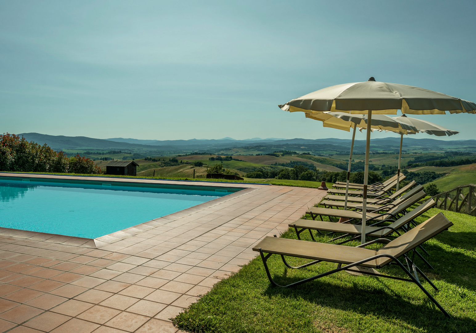 Infinity-Pool mit Sonnenliegen und freiem Blick über die Hügellandschaft und Felder.