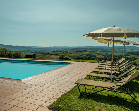 Infinity-Pool mit Sonnenliegen und freiem Blick über die Hügellandschaft und Felder.