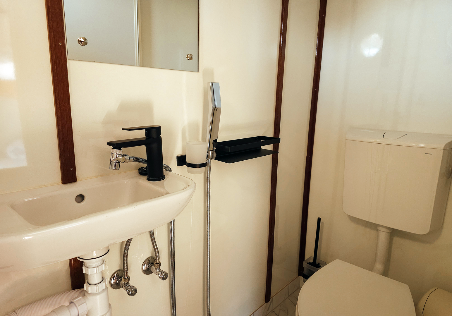 Kompaktes Bad mit Waschbecken, Dusche und WC in einer Schiffskabine.