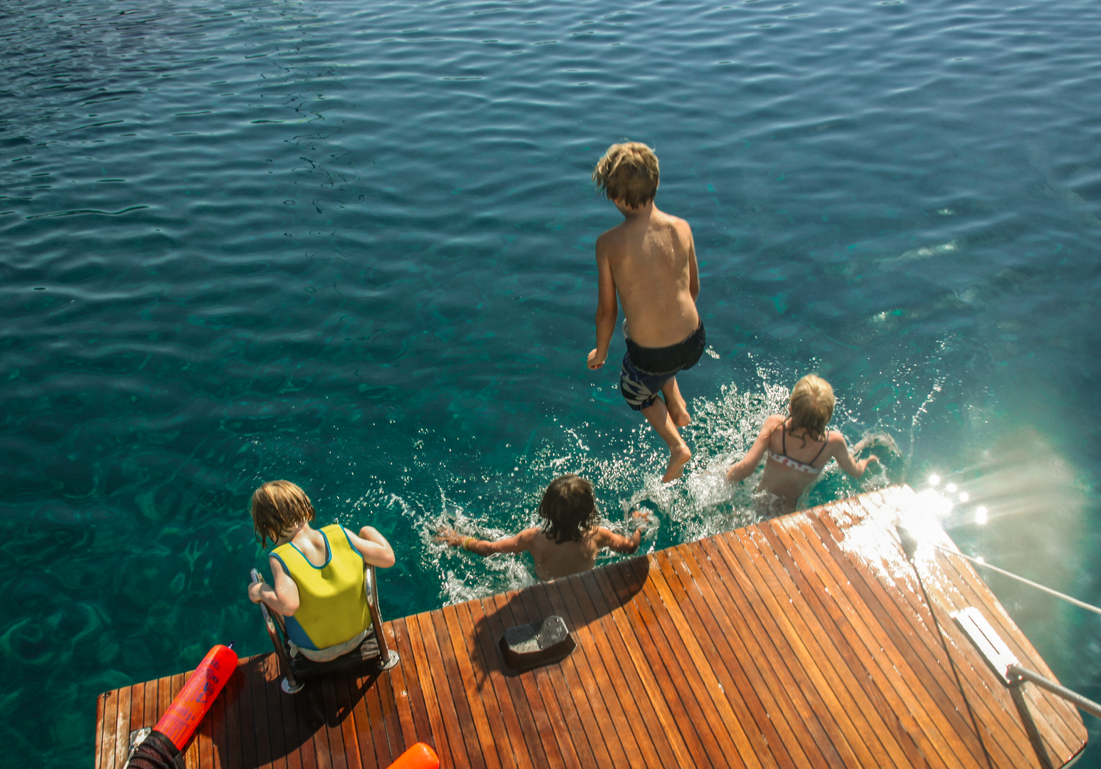Kinder springen von einer Badeplattform ins Meer.