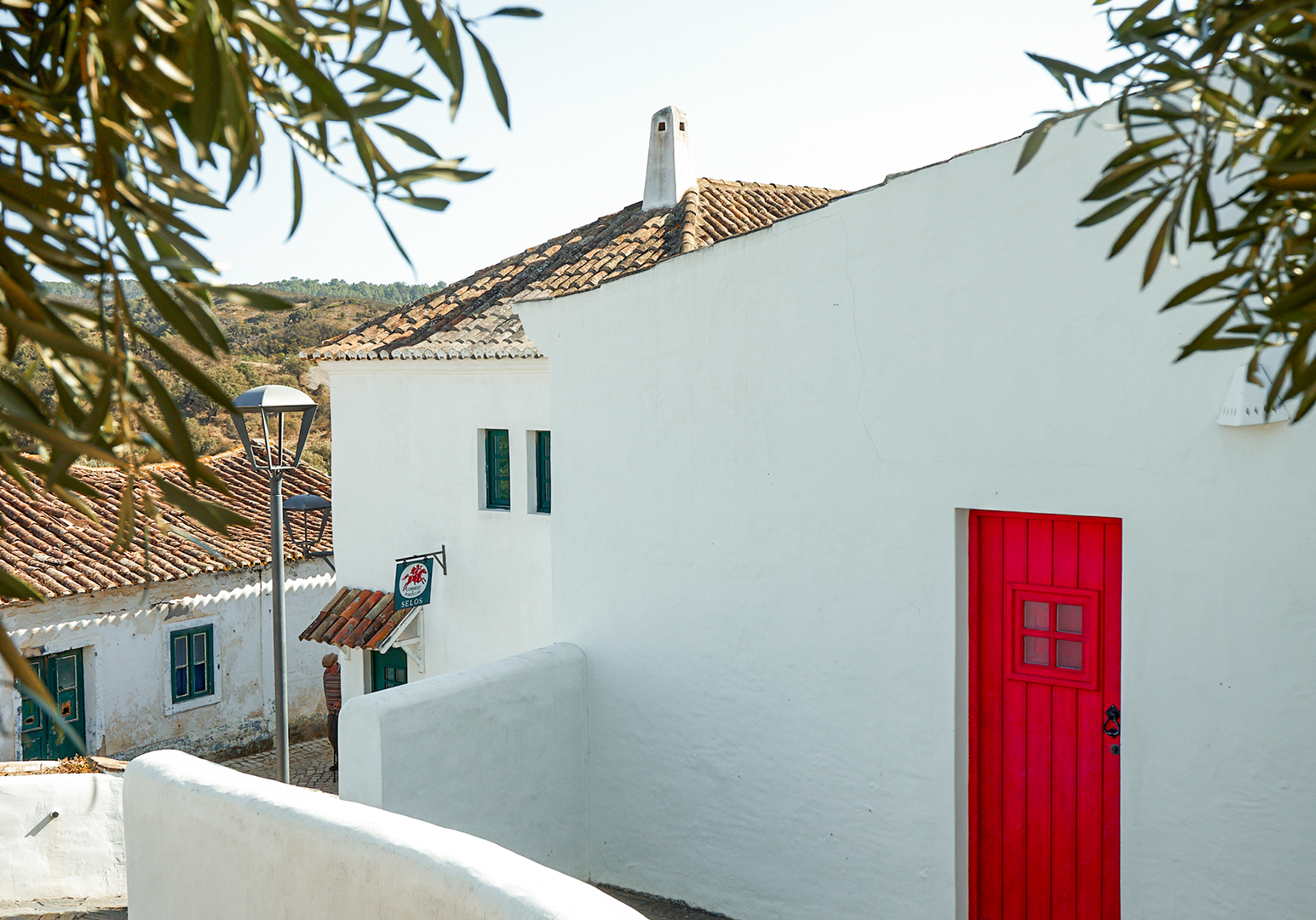 Schmale Gasse mit weißen Häusern und roten Türen in einem mediterranen Dorf.