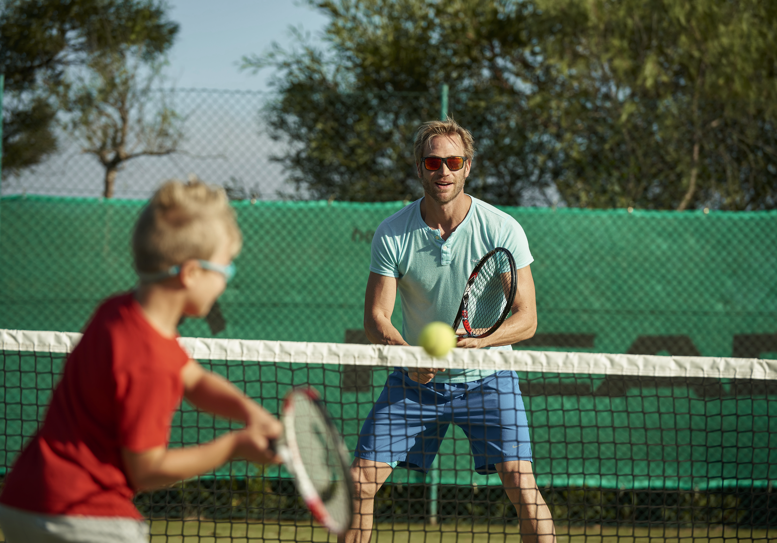 Vater und Kind spielen gemeinsam Tennis auf einem Outdoor-Tennisplatz.