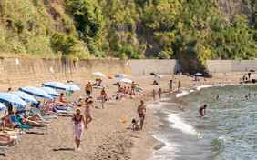 Der Strand an einer grün bewachsenen Felswand.