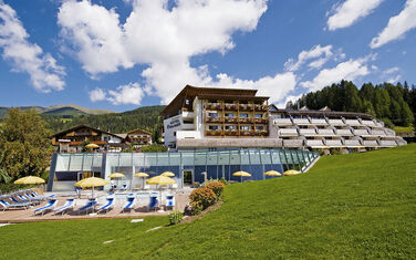 Das Family Resort Rainer in den Südtiroler Dolomiten, umgeben von grüßen Wiesen und einer beeindruckenden Bergkulisse.