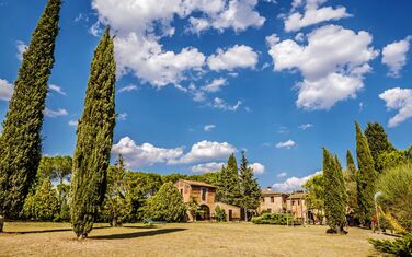 Garten und Gebäude eines Agriturismo in der Toskana mit Zypressen und anderen Bäumen